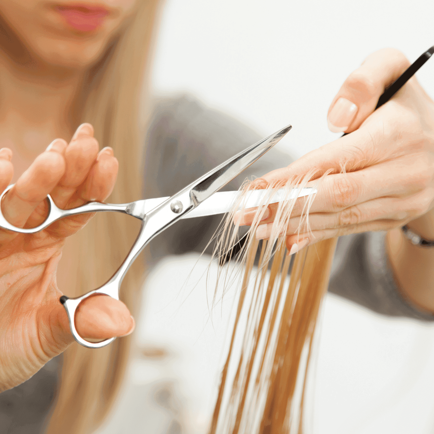 Hair being cut with scissors, close-up of hands and long blonde strands.