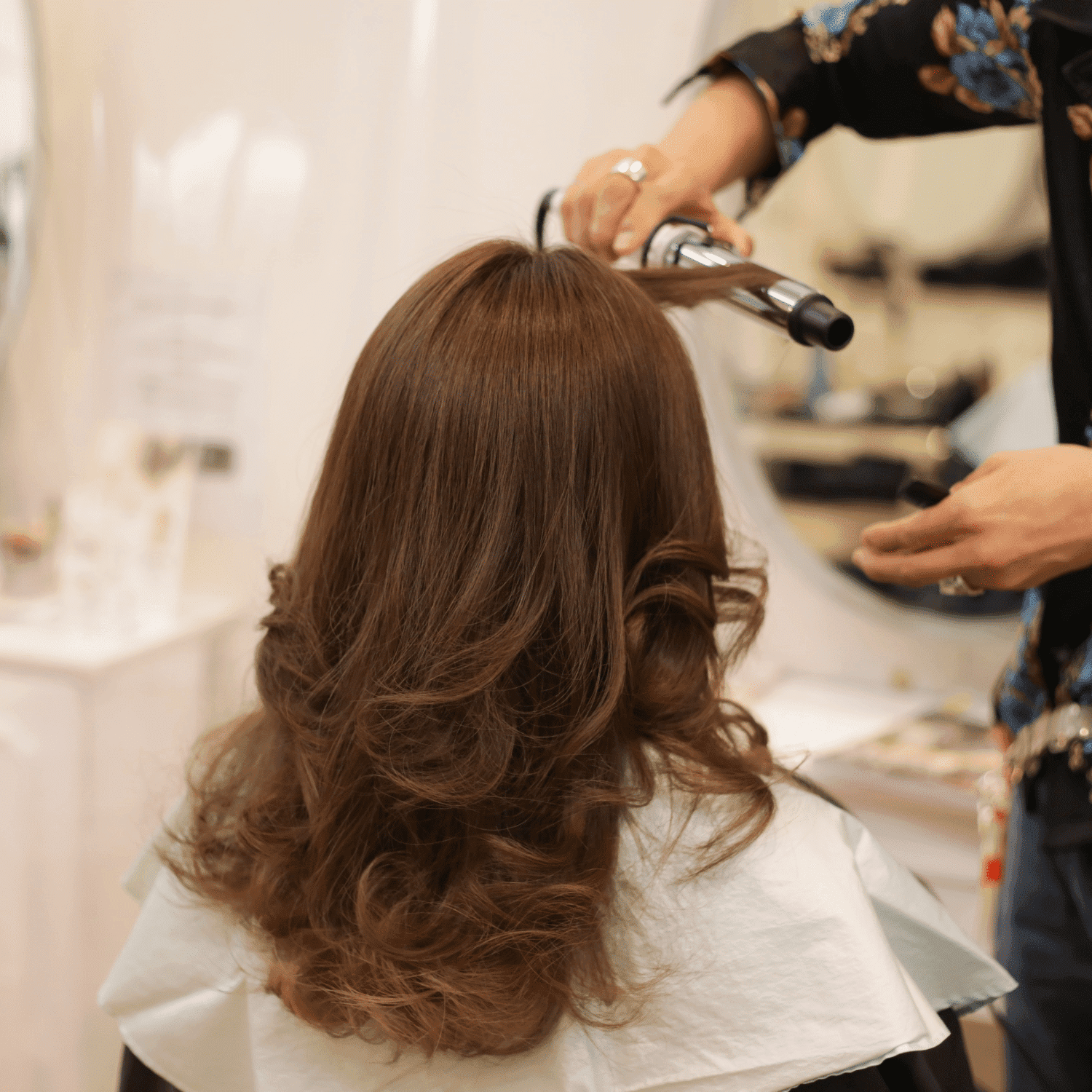 Stylist curling woman's hair in a salon, creating soft, voluminous waves.