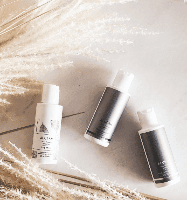 Minimalist skincare bottles on a marble surface with pampas grass decoration.